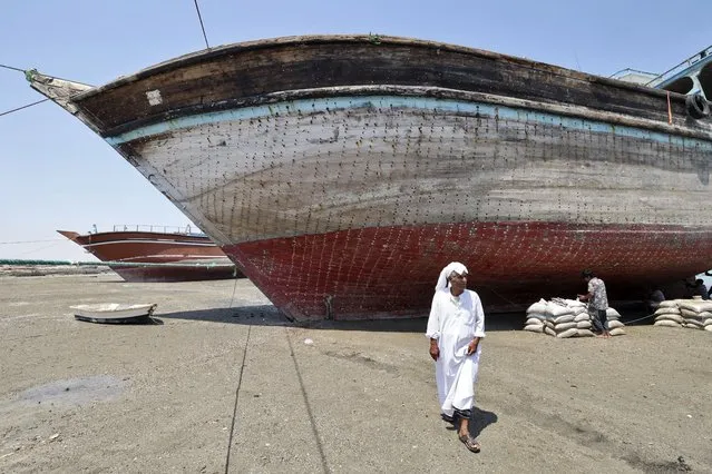 A man walks in front of a traditional wooden ships (lenj), laid ashore for restoration, in Iran's touristic Qeshm island in the Gulf, on April 29, 2023. From Muscat to Bandar Abbas via Dubai, the potbellied silhouette of the lenjs is part of the maritime landscape of the Middle East, just like that of the sailing dhows of the Arabian Peninsula. (Photo by Atta Kenare/AFP Photo)