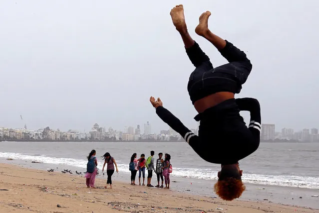 Beachgoers stroll as a boy practices somersaulting on a beach in Mumbai, India, July 12, 2018. (Photo by Danish Siddiqui/Reuters)