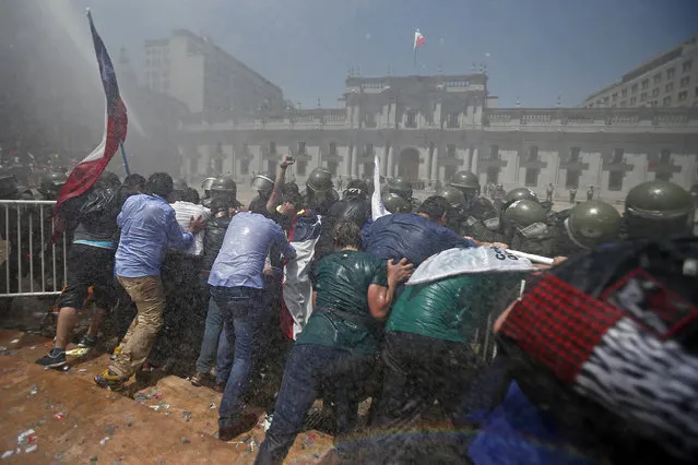 Public workers push against a police barrier and a water canon as they try to reach La Moneda presidential palace in Santiago, Chile, Thursday, November 17, 2016. Workers are upset with their salary increase, 3.2 percent, approved yesterday by Congress. Workers want a 4 percent increase, after lowering their demand from 7 percent. (Photo by Luis Hidalgo/AP Photo)