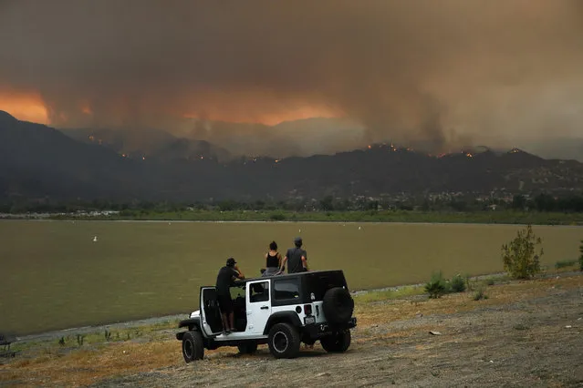Onlookers watch as a wildfire burns near Lake Elsinore, Calif., Wednesday, August 8, 2018. Evacuations have been ordered for several small mountain communities near where a forest fire continues to grow in Southern California. (Photo by Jae C. Hong/AP Photo)