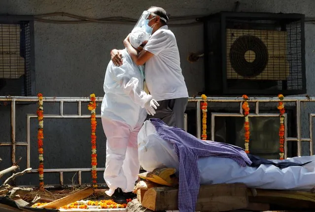 Relatives wearing personal protective equipment (PPE) mourn a man, who died from the coronavirus disease (COVID-19), next to his funeral pyre at a crematorium in New Delhi, India April 21, 2021. (Photo by Adnan Abidi/Reuters)