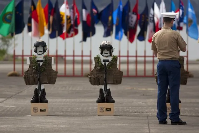 A U.S. Marine stands near the flight suits of two of the 12 Marines who died when their helicopters crashed off the North Shore of Oahu, Hawaii, during a memorial service on Friday January 22, 2016, at Marine Corps Base Hawaii. Servicemen draped flight gear on 12 white crosses Friday to commemorate the Marines who died when two helicopters crashed off the coast of Hawaii during a nighttime training mission. Military members and families gathered for the memorial service at Marine Corps Base Hawaii in Kaneohe after the status of the dozen missing Marines changed to deceased following five days of searching. (Photo by Caleb Jones/AP Photo)