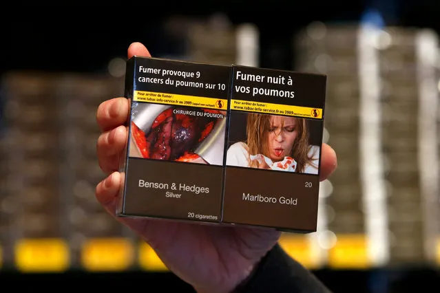 A tobacconist dispalys new cigarette packs, plain with unbranded packaging and the health warnings, “Smoking causes nine out of ten lung cancers” (L) and “Smoking harms your lungs” (R) as part of anti-smoking legislation in a French “Tabac” in Paris, France, January 2, 2017. Instead of advertising a brand, cigarette packs sport only health warnings and photos of illnesses caused by smoking. (Photo by Charles Platiau/Reuters)