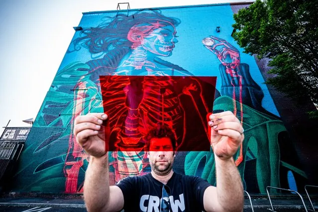 Organiser of “Upfest” Steve Hayles holds a red filter gel beside a graffiti piece by artist Insane 51, which is an interactive piece and can be viewed differently through either a blue or a red filter, like the ones in 3D glasses, revealing a woman or the skeleton within her body, on a huge wall in Bedminster, Bristol on Wednesday July 21, 2021, as the 75 murals project reaches the halfway point and various graffiti pieces are sprayed onto walls and buildings across the city over the Summer. (Photo by Ben Birchall/PA Images via Getty Images)