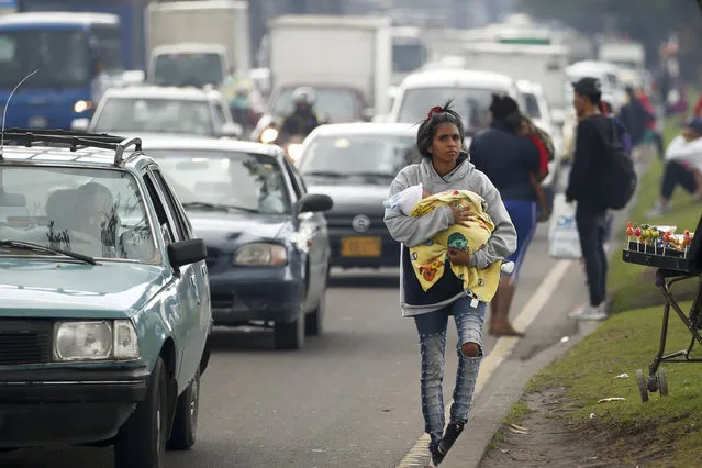 A Venezuelan migrant, cradling a baby, walks along an avenue where she asks drivers for their spare change, in Bogota, Colombia, Thursday, April 4, 2019. According to U.N. children's agency UNICEF, as a result of the Venezuela migrant crisis, 1.1 million children will need help across Latin America and the Caribbean in 2019. (Photo by Fernando Vergara/AP Photo)