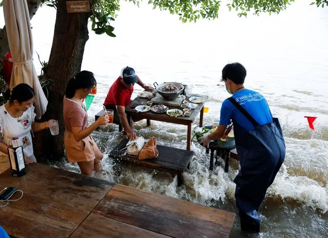 People eat food at a flooded restaurant, where patrons stand up from their tables every time the waves come in, on a river bank in Nonthaburi near Bangkok, Thailand, October 7, 2021. Videos have gone viral on social media of customers sitting on drenched chairs, taking mouthfuls of food as long-tail boats buzz by, then moving out of the way as waves hit. (Photo by Soe Zeya Tun/Reuters)