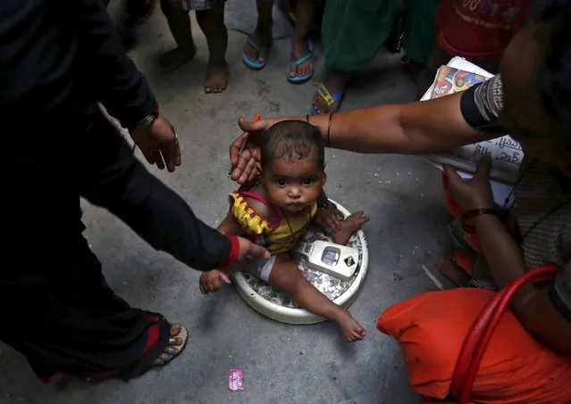 A health worker (R) weighs a child under a government program in New Delhi, India, May 7, 2015. As Prime Minister Narendra Modi completes one year in office, his cuts in federal welfare spending on the poorest of India's 1.25 billion people are coming in for sharp criticism, including from within his cabinet. (Photo by Anindito Mukherjee/Reuters)