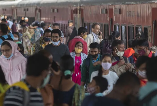 Passengers arrive wearing face masks at a train station in Mumbai, India, Thursday, December 23, 2021. The government on Thursday in a review meeting cautioned states to observe all precautions and don't let the guard down in view of the rise in Omicron variant cases. (Photo by Rafiq Maqbool/AP Photo)