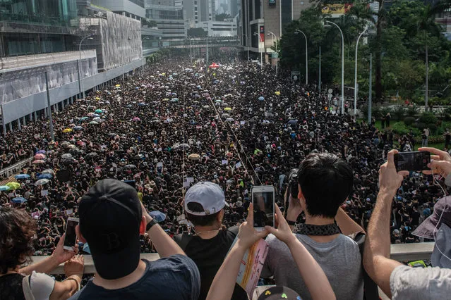 People take photographs as protesters match on the road below beneath during a demonstration against the now-suspended extradition bill on June 16, 2019 in Hong Kong. Large numbers of protesters rallied on Sunday despite an announcement yesterday by Hong Kong's Chief Executive Carrie Lam that the controversial extradition bill will be suspended indefinitely. (Photo by Carl Court/Getty Images)