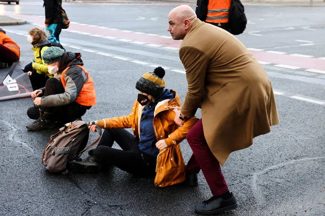A man removes a “Letzte Generation” (Last Generation) activist who blocks the exit of a highway to protest against food waste and call for an agricultural change to reduce greenhouse gas emissions, in Berlin, Germany, February 7, 2022. (Photo by Christian Mang/Reuters)
