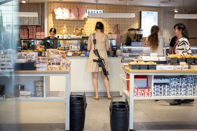 A woman with a rifle shops in a bakery, amid the ongoing conflict between Israel and Hamas, in Tel Aviv, Israel, on June 4, 2024. (Photo by Marko Djurica/Reuters)