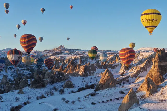 Hot-air balloons glide over snow covered fairy chimneys in the Cappadocia in Goreme district of Nevsehir, Turkiye on February 11, 2022. Cappadocia is one of the vital tourism regions of Turkiye. Tourists join the hot air balloon tour and watch the natural beauties from the sky. It is considered the center of hot air ballooning globally, as it can fly 250 days a year. Cappadocia on the UNESCO World Heritage List receives tourists from various countries for 12 months. Last year, 388,833 tourists participated in hot air balloon tours in Cappadocia. (Photo by Behcet Alkan/Anadolu Agency via Getty Images)