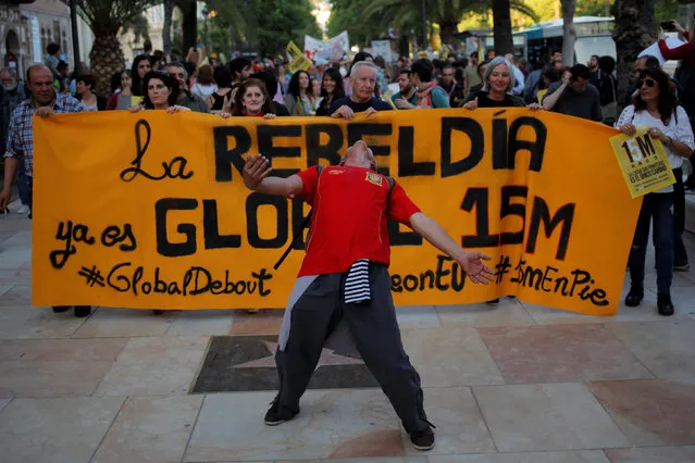 Jose Ruiz, 57, a homeless man, wearing a Spanish national soccer shirt, dances as he attends a march to mark the 5th anniversary of the “indignados” movement in Malaga, Spain, May 15, 2016. The banner reads, “The rebellion is now global. 15M”. (Photo by Jon Nazca/Reuters)