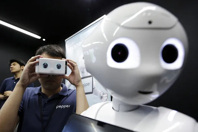 An attendant holds a Google Inc. Cardboard virtual reality headset to demonstrate SoftBank Group Corp.'s Pepper the humanoid robot at a media briefing in Tokyo, Japan, on Thursday, May 19, 2016. Developers will now be able to build Pepper apps using Android tools, SoftBank announced on Thursday. (Photo by Kiyoshi Ota/Bloomberg)