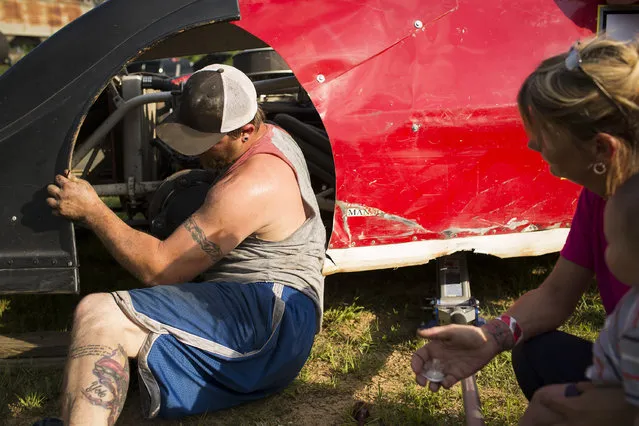 In this July 17, 2015 photo, Jeremy Thomasson reaches through a wheel well to fix a steering problem during dirt track racing at the Ponderosa Speedway in Junction City, Ky. His mother, Natalie Johnson, right, holds his son Ayden Ward so they can see and help if needed. (Photo by David Stephenson/AP Photo)