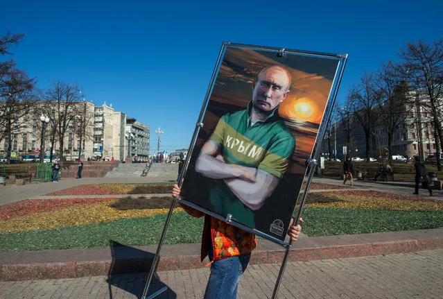 A man carries a picture depicting Russia's President Vladimir Putin in a T-shirt with an inscription reading: “Crimea” at an open-air political cartoons exhibition dedicated to the one-year anniversary of Crimea voting to leave Ukraine and join the Russian state in central Moscow on March 16, 2015. (Photo by Dmitry Serebryakov/AFP Photo)