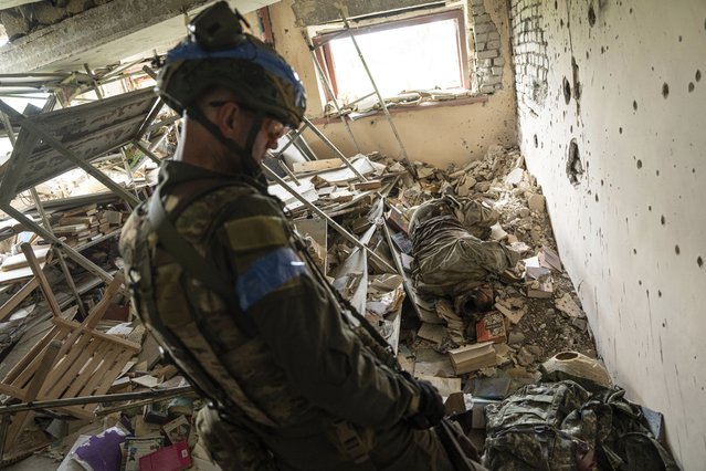 A Ukrainian commander, aka Lermontov, of the 68th Oleksa Dovbush hunting brigade, walks past the body of a killed Russian soldier in the recently retaken village of Blahodatne, Ukraine, Saturday, June 17, 2023. (Photo by Evgeniy Maloletka/AP Photo)