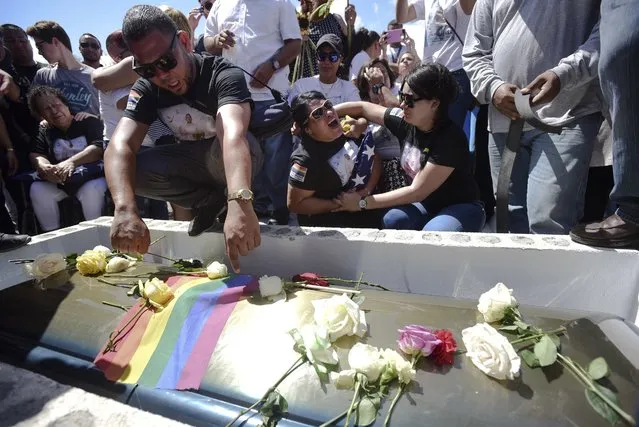 Accompanied by grieving family members, Luis Angel Candelario bids farewell to his brother Angel Candelario Padro, a 28-year-old nurse and National Guard member, at his graveside at the Guanica municipal cemetery in Puerto Rico, Saturday, June 18, 2016. Angel Candelario Padro was one of 49 persons slain in the mass shooting at a nightclub in Orlando, Fla. The ceremony for Candelario was one of several being held on the island this week for victims of the Orlando attack. (Photo by Carlos Giusti/AP Photo)