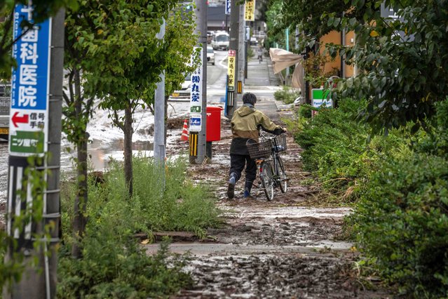 A man pushes his bicycle along a muddy sidewalk following heavy rain in Wajima city of Ishikawa prefecture on September 22, 2024. Heavy rain lashed central Japan on September 22, with floods and landslides leaving one dead and at least six missing in an area already devastated by a major earthquake this year. (Photo by Yuichi Yamazaki/AFP Photo)