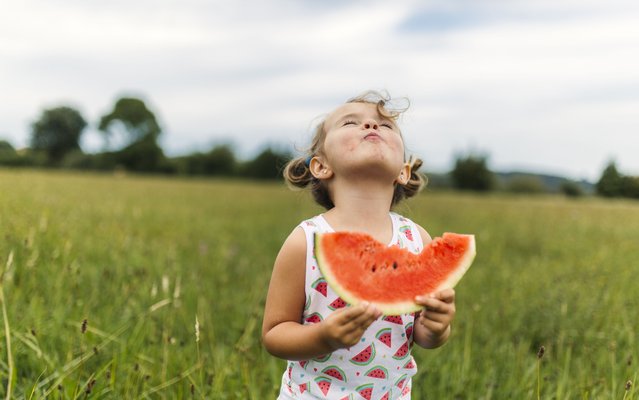 Little girl eating watermelon on a meadow. (Photo by Westend61/Getty Images)