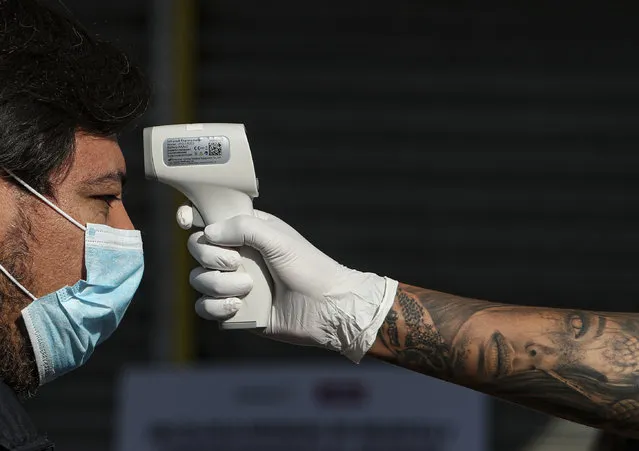 A city worker measures the temperature of a man before entering the Apumanque shopping center in Las Condes neighborhood,  in Santiago, Chile, Thursday, April, 30, 2020. As Chilean authorities look to ease COVID-19 related quarantine measures, the well-known shopping mall in the upscale neighborhood opened to the public for the first time on Thursday since lockdown began over one month ago. (Photo by Esteban Felix/AP Photo)