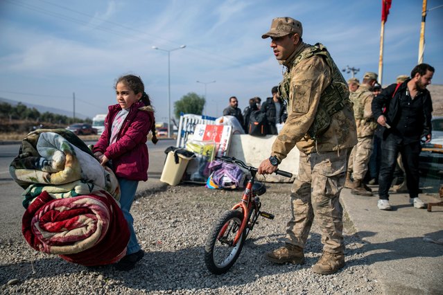 A Turkish gendarme helps a young girl with belongings as Syrian families wait to cross into Syria from Turkey at the Cilvegozu border gate near the town of Antakya, southern Turkey, Tuesday, December 10, 2024. (Photo by Metin Yoksu/AP Photo)