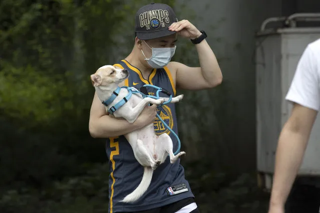 A man wearing a mask carries his dog along a street in Beijing on Thursday, June 25, 2020. In China, where the virus first appeared late last year, an outbreak in Beijing appeared to have been brought under control. (Photo by Ng Han Guan/AP Photo)
