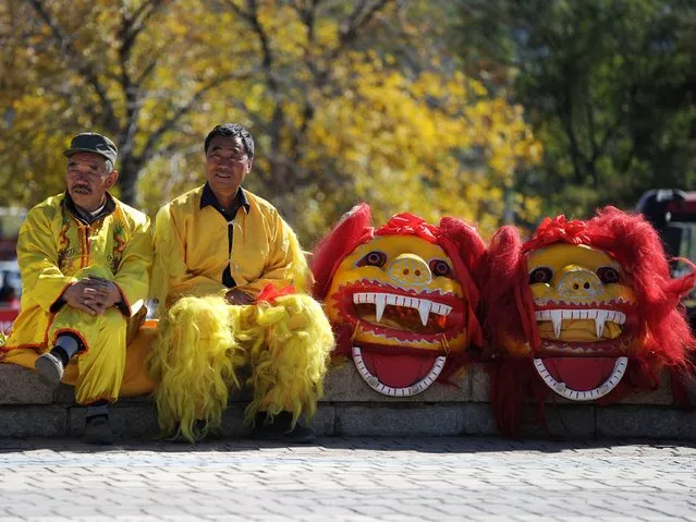 Two Chinese men wait to perform a lion dance at the start of the fourth stage of the 2014 Tour of Beijing cycling race in the suburbs of Beijing on October 13, 2014. The 2014 Tour of Beijing kicked off from the Zhangjiakou, in China's Hebei Province on October 10 with five stages throughout the capital city ending in the Bird's Nest Piazza on October 14. (Photo by Wang Zhao/AFP Photo)