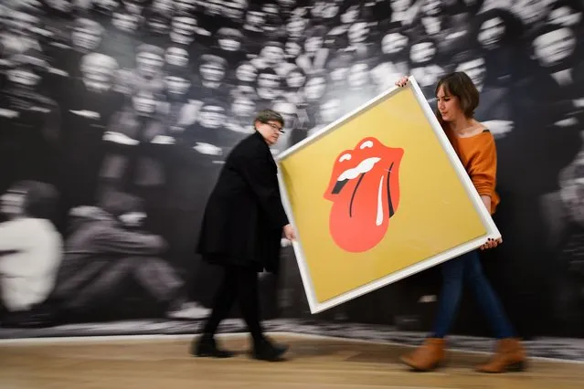 Gallery assistants pose for pictures with John Pasche's 1971 “Tongue and Lip Design” logo, commissioned by Mick Jagger, at a photocall for a retrospective of students' artwork, titled “GraphicsRCA: Fifty Years” at the Royal College of Arts in London, on November 4, 2014. (Photo by Leon Neal/AFP Photo)