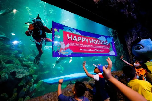 Diver Fachri Hariansyah, 26, dressed in Santa Claus costume, waves to children during a show on Christmas celebrations at the Sea World Ancol aquarium in Jakarta, Indonesia, December 25, 2022. (Photo by Willy Kurniawan/Reuters)