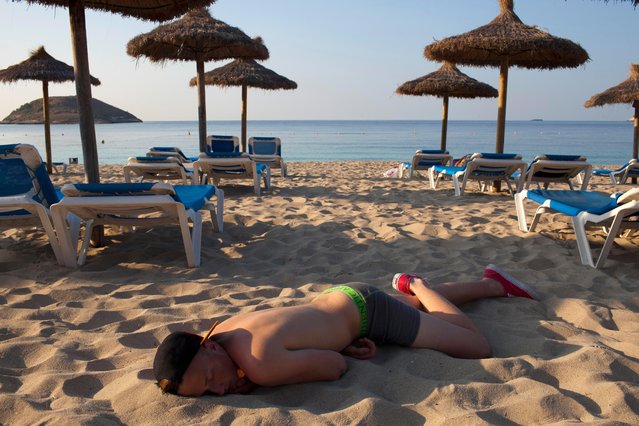 A British man wearing a BCM club hat and his underpants slumped face down in the sand on Magaluf beach, Majorca, Spain on June 29, 2013. (Photo by Peter Dench/Getty Images Reportage)