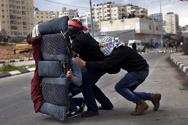 Masked Palestinians use a car seat as a shield during a protest to support four imprisoned Palestinians on a hunger strike, outside Ofer, an Israeli military prison near the West Bank city of Ramallah, February 19, 2013. (Photo by Bernat Armangue/Associated Press)
