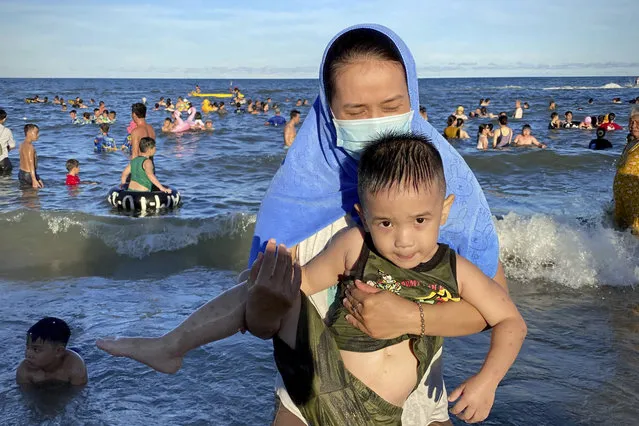 A woman wearing a mask carries her child on a beach in Vung Tau city, Vietnam, Sunday, July 26, 2020. Vietnam on Sunday reimposed restrictions in one of its most popular beach destinations after a second person tested positive for the virus, the first locally transmitted cases in the country in over three months. (Photo by Hau Dinh/AP Photo)