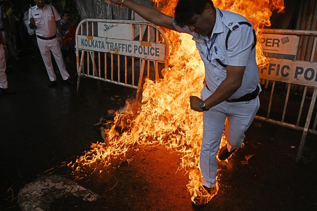 A police officer reacts after his shoes caught fire while trying to douse a fire set by leftist activists on an effigy of India's Prime Minister Narendra Modi, at a rally in Kolkata on July 9, 2025, during a nationwide general strike called by the trade unions against what they say are the government's anti-worker policies. (Photo by Dibyangshu Sarkar/AFP Photo)