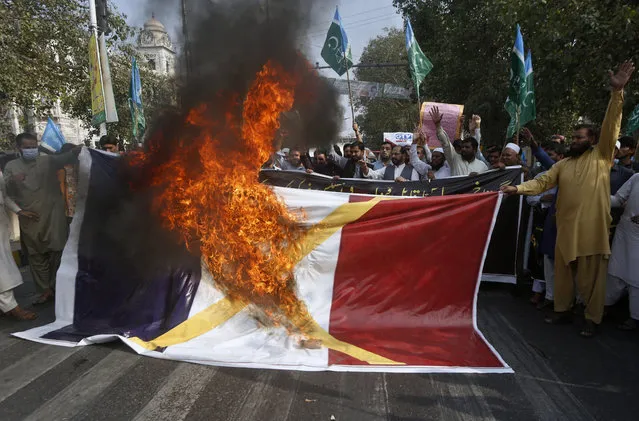 Supporters of religious group burn a representation of a French flag during a rally against French President Emmanuel Macron and republishing of caricatures of the Prophet Muhammad they deem blasphemous, in Lahore, Pakistan, Friday, October 30, 2020. Muslims have been calling for both protests and a boycott of French goods in response to France's stance on caricatures of Islam's most revered prophet. (Photo by K.M. Chaudary/AP Photo)