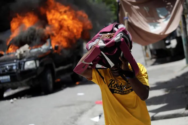 A man covers himself with a backpack as he runs past a burning car during a protest following a march organised by lawyer organisations to demand justice on the killing of lawyer and President of the Bar of Lawyers of Port-au-Prince Monferrier Dorval, in the streets of Port-au-Prince, Haiti on September 3, 2020. (Photo by Andres Martinez Casares/Reuters)