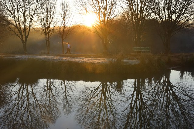 A woman walks in the Emmarentia Park as tress are reflected in a dam and frost covers the ground, in Johannesburg, South Africa, 11 July 2025. Winter temperatures drops to well below zero degrees Celsius at nights as Johannesburg sits at 1750m above sea level. This combined with low winter temperatures causes the frost layers through out the city. (Phoot by Kim Ludbrook/EPA)