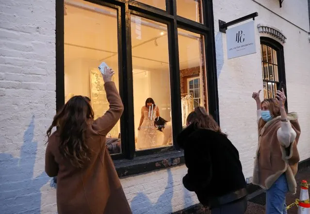 Alana Pines, (center), tries on a potential wedding dress as her sister, Danielle Pines, cousin, Ari Goret, and aunt, Jill Goret, react from the sidewalk outside as the global outbreak of the coronavirus disease (COVID-19) continues, in New York City, U.S., November 14, 2020. (Photo by Caitlin Ochs/Reuters)
