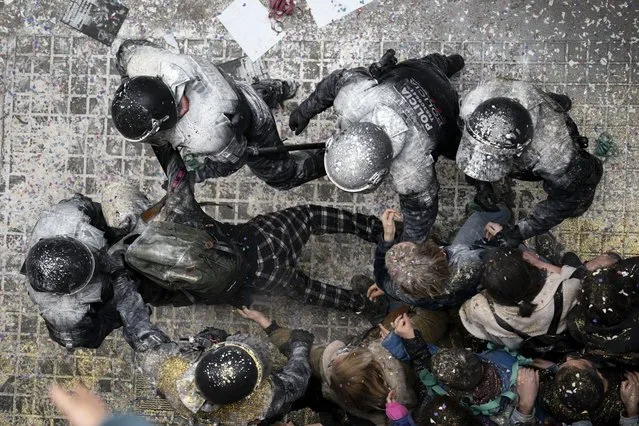 Riot police officers covered in flour that was thrown at them, detain an anti-evictions activist before breaking into Ganna Drozdovych's apartment to evict her and her family from their apartment for non-payment rent in Barcelona, Spain, Monday, February 14, 2022. Ganna Drozdovych, 48, a a hotel worker who was on a furlough temporary workforce reduction program during the pandemic was evicted along with her unemployed partner and two sons. (Photo by Joan Mateu Parra/AP Photo)