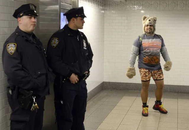 A participant in the No Pants Subway Ride waits for a train next to police officers in New York subway on January 11, 2015 in New York. (Photo by Timothy A. Clary/AFP Photo)