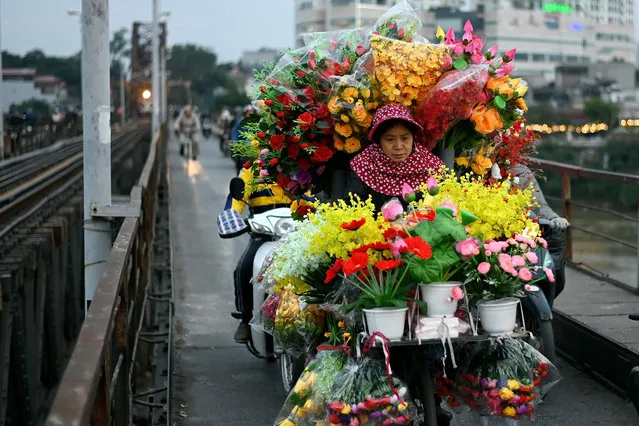 A woman selling artificial flowers rides her bicycle along the Long Bien bridge in Hanoi on January 12, 2021. (Photo by Manan Vatsyayana/AFP Photo)