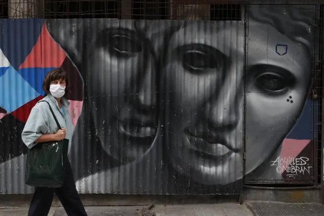 A woman wearing a face mask to protect from the spread of coronavirus, stands in front of a graffiti by the Greek artist Achilles in Athens, Tuesday, April 6, 2021. Lockdown measures have been in force since early November but an ongoing surge in COVID-19 infections remains high as the country battles to emerge from deep recession. (Photo by Thanassis Stavrakis/AP Photo)