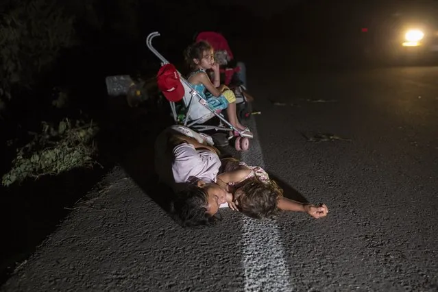 Sleeping on the asphalt, a migrant mother and her daughters wait for a free ride on the shoulder of the highway, between Pijijiapan and Arriaga, Mexico, Friday, October 26, 2018. In the migrant caravan currently in southern Mexico, it's particularly tough for children and families who are trying to keep things together after more than two weeks on the road. (Photo by Rodrigo Abd/AP Photo)
