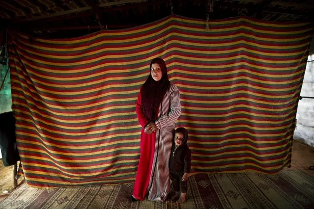 In this Monday, March 16, 2015 photo, Syrian refugee Shams Alhamadah, 24, who is two months pregnant with her fifth child, poses for a portrait with her son Ismail inside their tent at an informal tented settlement near the Syrian border, on the outskirts of Mafraq, Jordan. (Photo by Muhammed Muheisen/AP Photo)