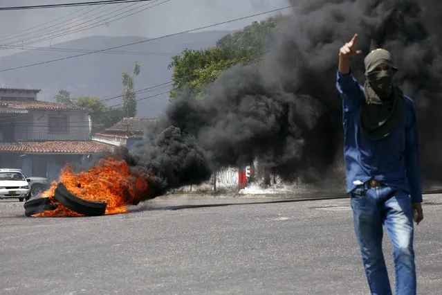 An anti-government protester walks in front of burning tires on a street in San Cristobal, in the state of Tachira, Venezuela on February 12, 2016. (Photo by Carlos Eduardo Ramirez/Reuters)