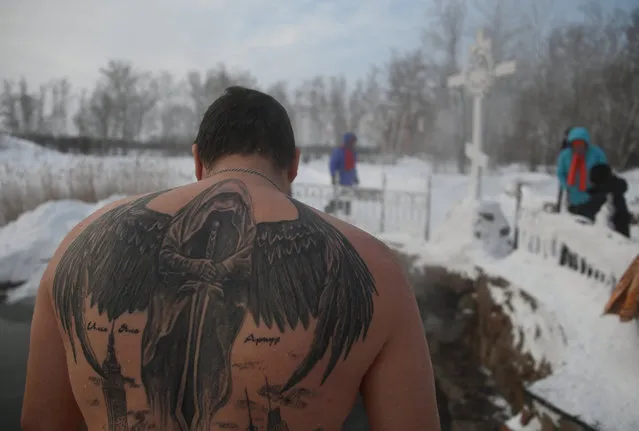 A man with a tattoo on his back stands near a font with icy water during celebrations of the Orthodox Christian feast of Epiphany at the Achairsky Monastery in the Omsk Region, Russia on January 19, 2024. (Photo by Alexey Malgavko/Reuters)