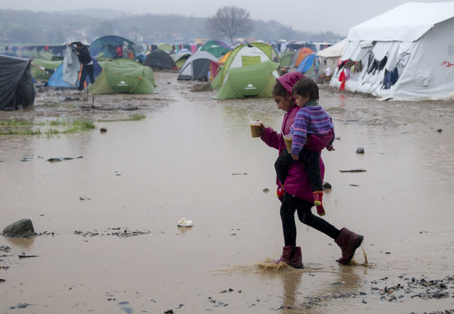 A girl walks by large puddles carrying a baby and rations of hot soup during a heavy rain at the northern Greek border station of Idomeni, Wednesday, March 9, 2016.  Northbound borders are closed and authorities plan to distribute fliers telling refugees seeking to reach central Europe that “there is no hope of you continuing north, therefore come to the camps where we can provide assistance” as more than 36,000 transient migrants are thought to be stuck in financially struggling Greece. (Photo by Vadim Ghirda/AP Photo)