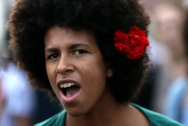 A woman, wearing a red carnation in her hair, sings a protest song during a march marking the international May Day, in Lisbon, Friday, May 1, 2015. (Photo by Francisco Seco/AP Photo)