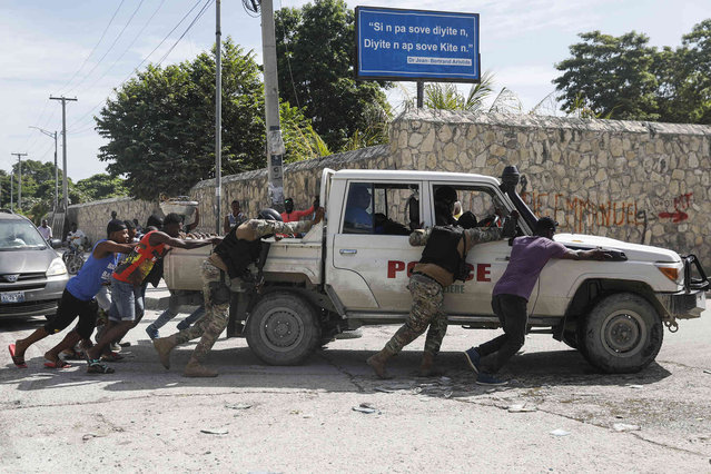 People push a police car that ran out of gas, in Port-au-Prince, Haiti, Wednesday, October 27, 2021. (Photo by Joseph Odelyn/AP Photo)