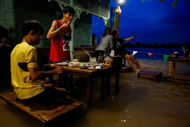 People eat food at a flooded restaurant, where patrons stand up from their tables every time the waves come in, on a river bank in Nonthaburi near Bangkok, Thailand, October 7, 2021. Restaurant owner Titiporn Jutimanon was convinced a bout of flooding in Thailand could be the end of a business already struggling from the pandemic. But with the rising tide of the Chao Phraya river this week came an unexpected opportunity. (Photo by Soe Zeya Tun/Reuters)